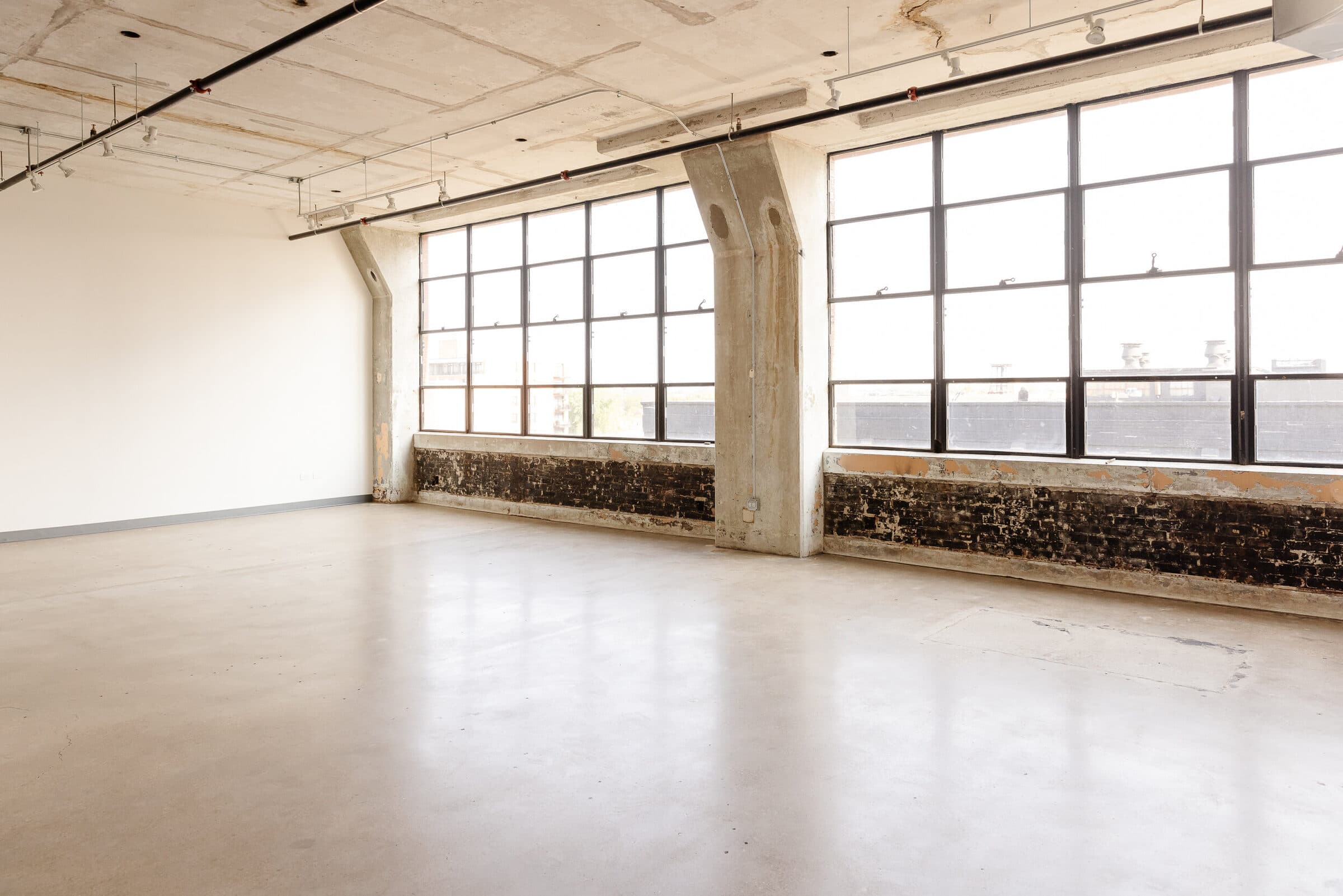 The empty studio: steel-framed windows above a brick band, concrete columns, and a concrete floor