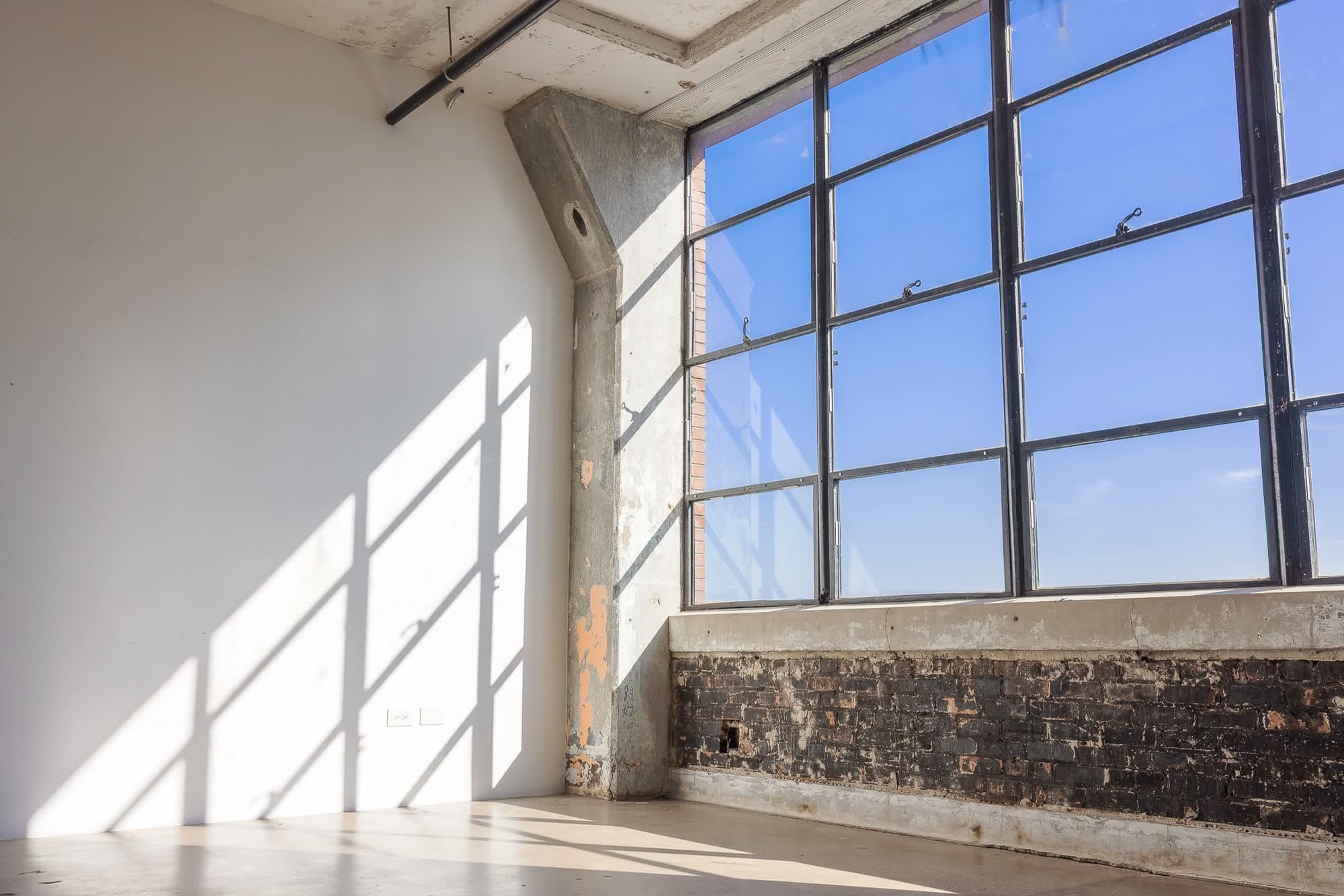 Midday sun through the south-facing windows, the window grid thrown in long bars across the white wall